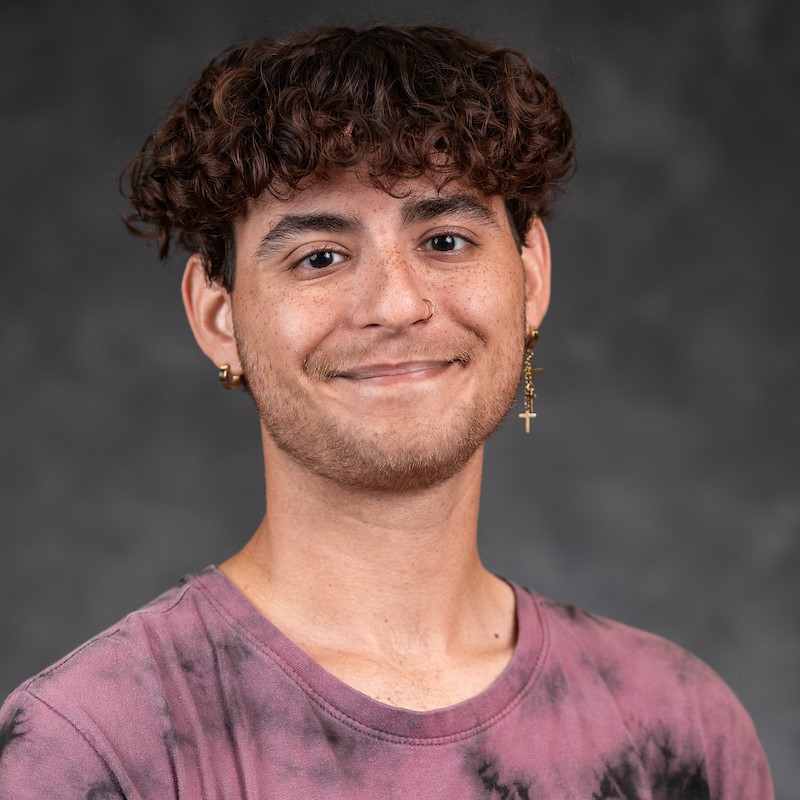 Man with short hair and earrings smiling