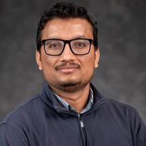 Man in glasses and grey collared shirt half smiling
